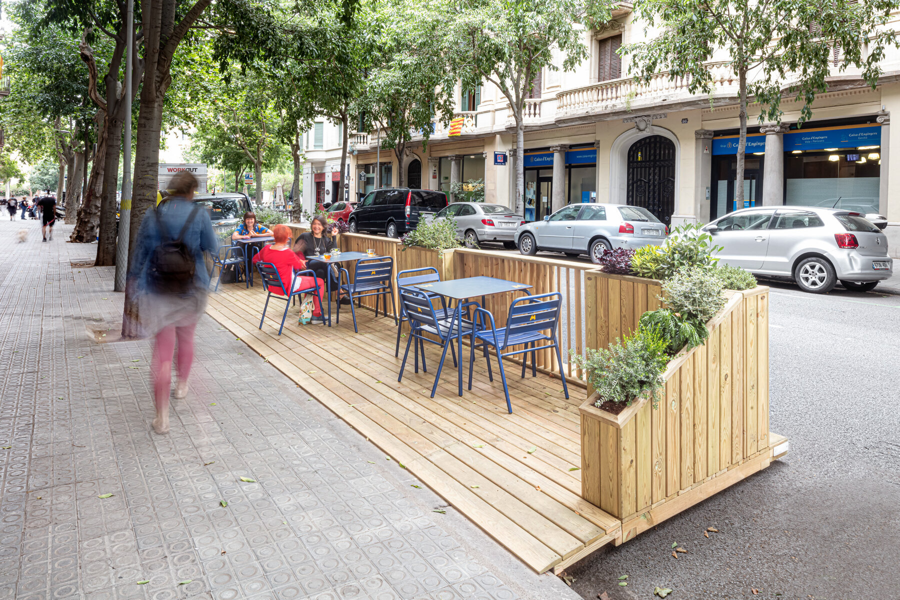 Reconfigurable wooden EcoParklet modules with integrated planting enable outdoor dining in a former parking bay.