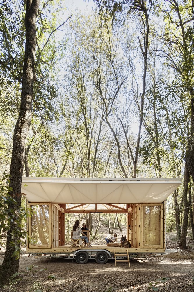 Awning raised, gathered around the mobile venue in the forest.