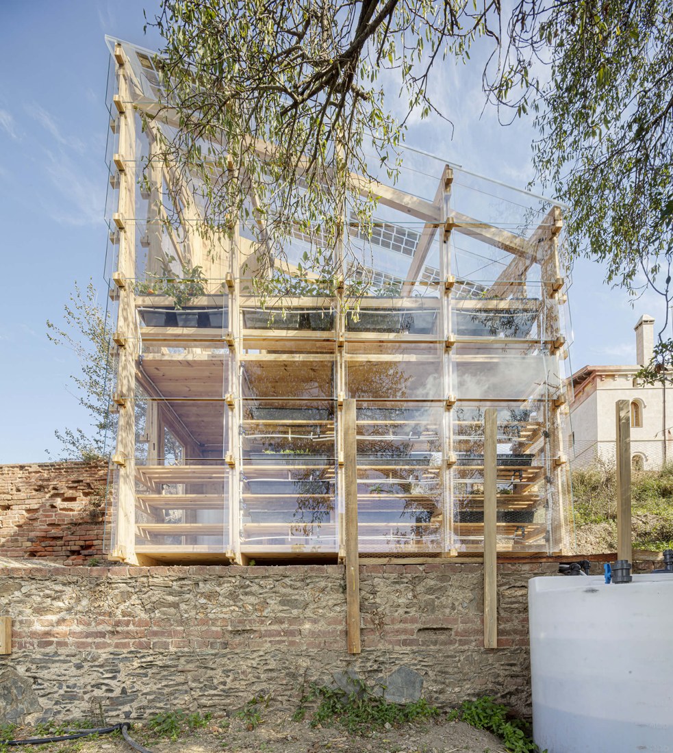 The timber and glass materiality of the greenhouse juxtaposes with the historic brick and stone masonry wall below.